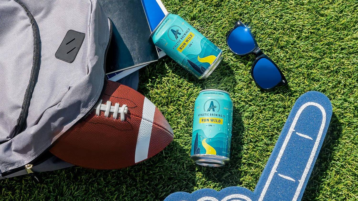 Tailgate flatlay with a football, backpack, and non-alcoholic beer cans
